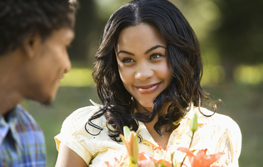 Pretty African American woman holding flower bouquet smiling at man outdoors.